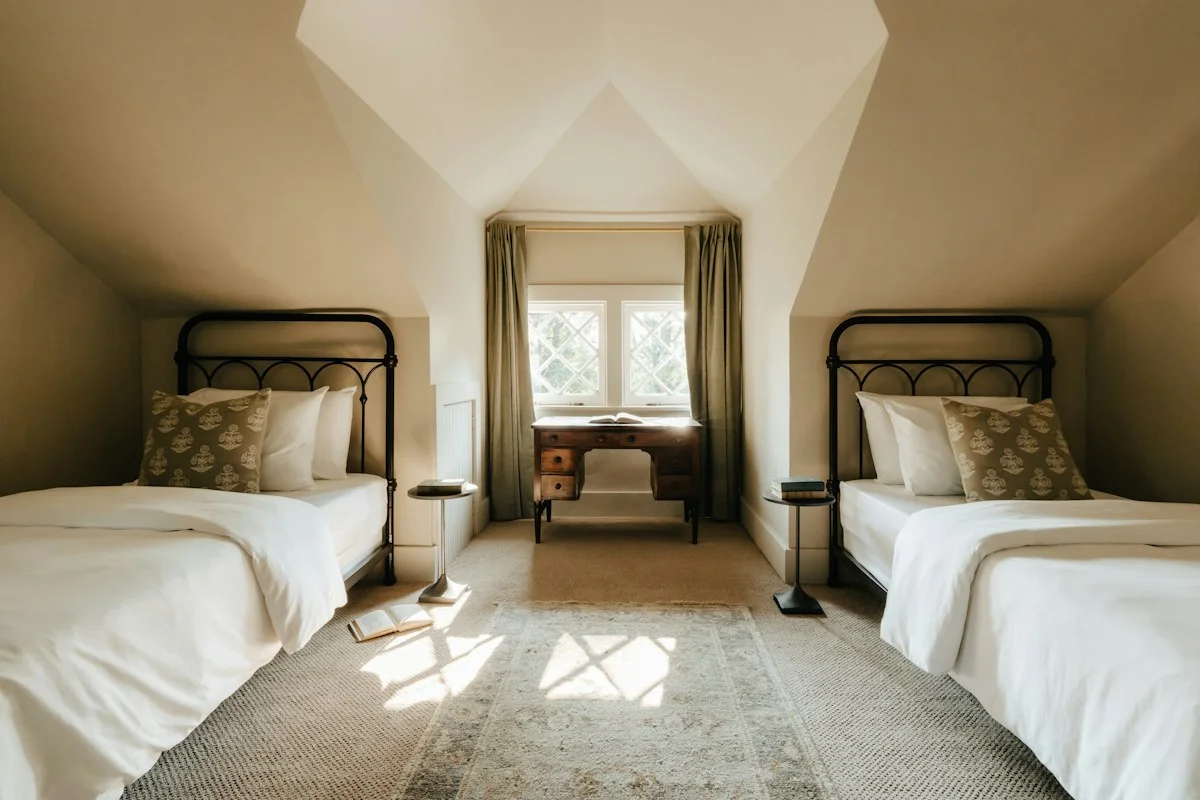 Two beds either side of a dormer window in a sunlit attic room