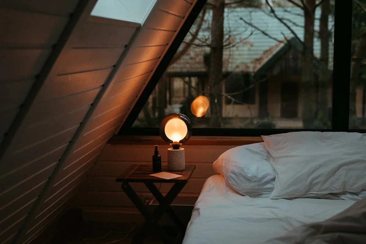 A lamp-lit double bed under the sloping timber roof
